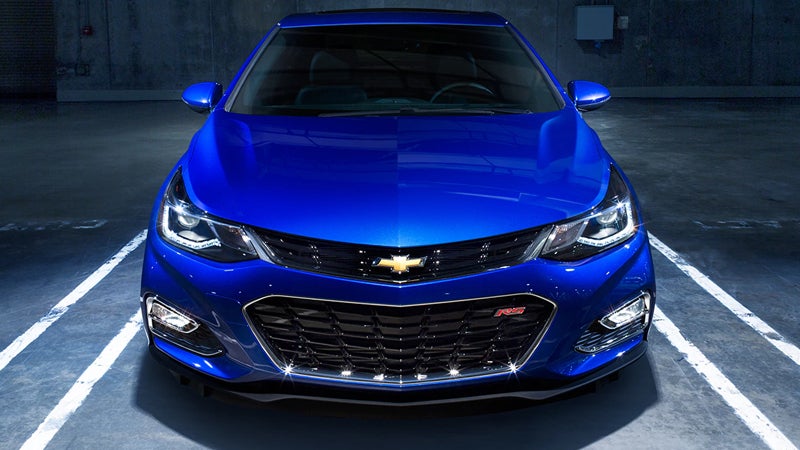 A front view of a blue Chevrolet Cruze parked in a marked parking space at night