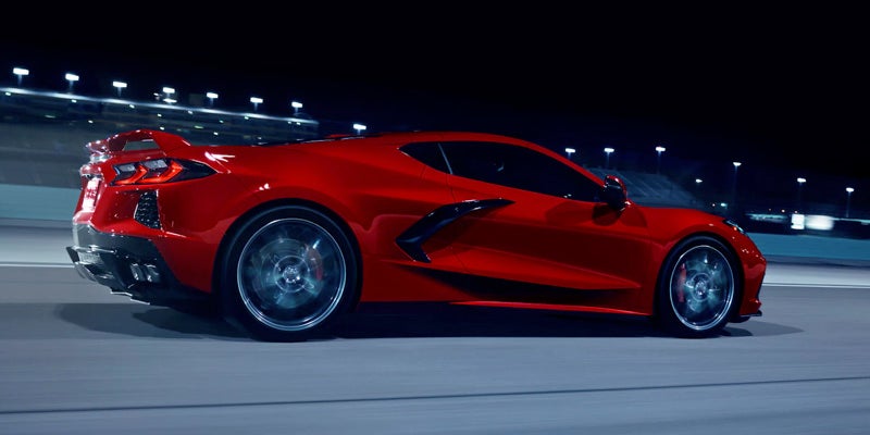 A red Chevrolet Corvette Stingray parked under blue neon lights at night