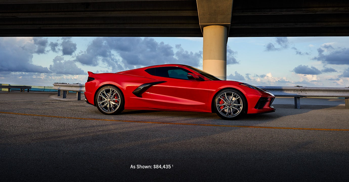 A red 2024 Chevrolet Corvette Stingray parked near a highway underpass at sunset