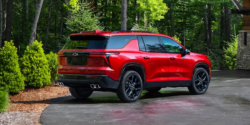 A red 2024 Chevrolet Traverse parked in a wooded area with green trees in the background