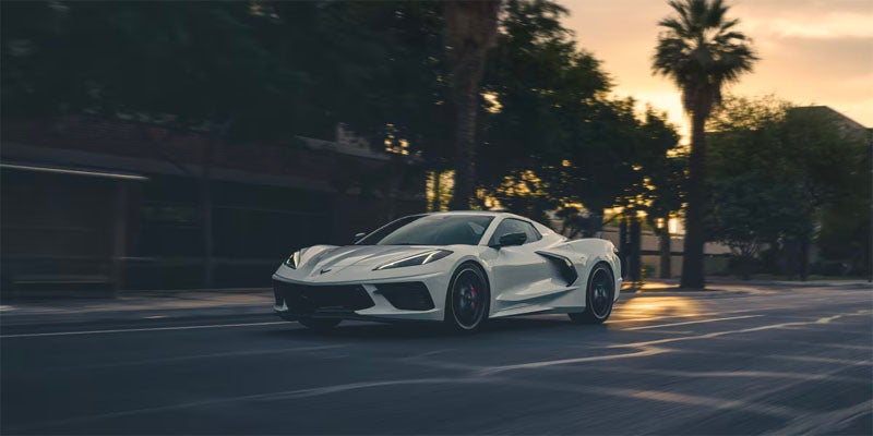 A white 2025 Chevrolet Corvette Stingray parked on a road with palm trees in the background