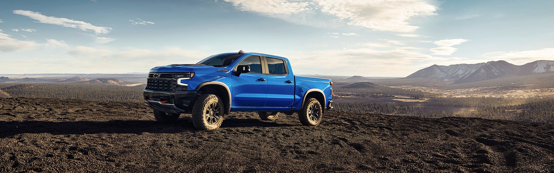A blue 2025 Chevrolet Silverado 1500 parked on rugged terrain with mountains in the background