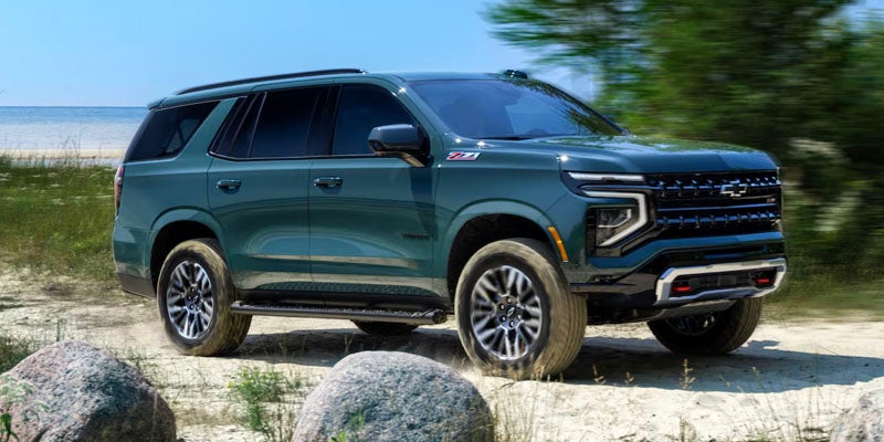 A green 2025 Chevrolet Tahoe parked on a sandy road with rocks and greenery nearby