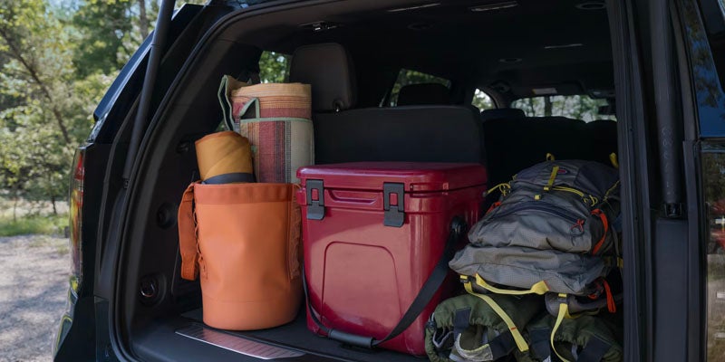 The open trunk of the 2025 Chevrolet Tahoe, packed with camping and outdoor gear, including a cooler and backpacks