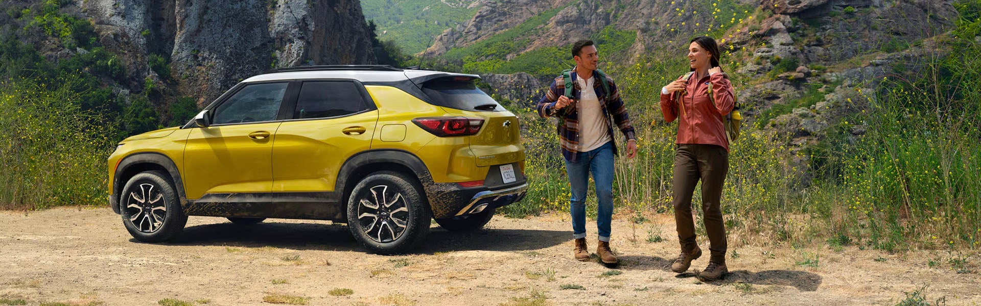 Yellow 2025 Chevrolet Trailblazer parked beside hills with a couple standing near the car